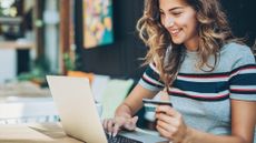 A smiling young woman is holding a credit card and typing on a laptop