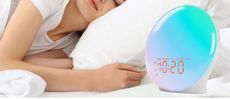 The image shows the JALL sunrise alarm clock on a bedside table in a bedroom 