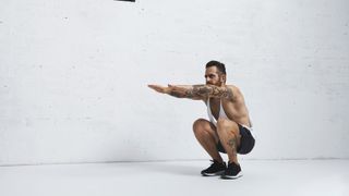 Man in a low squat with arms extended at shoulder height during gorilla walk exercise